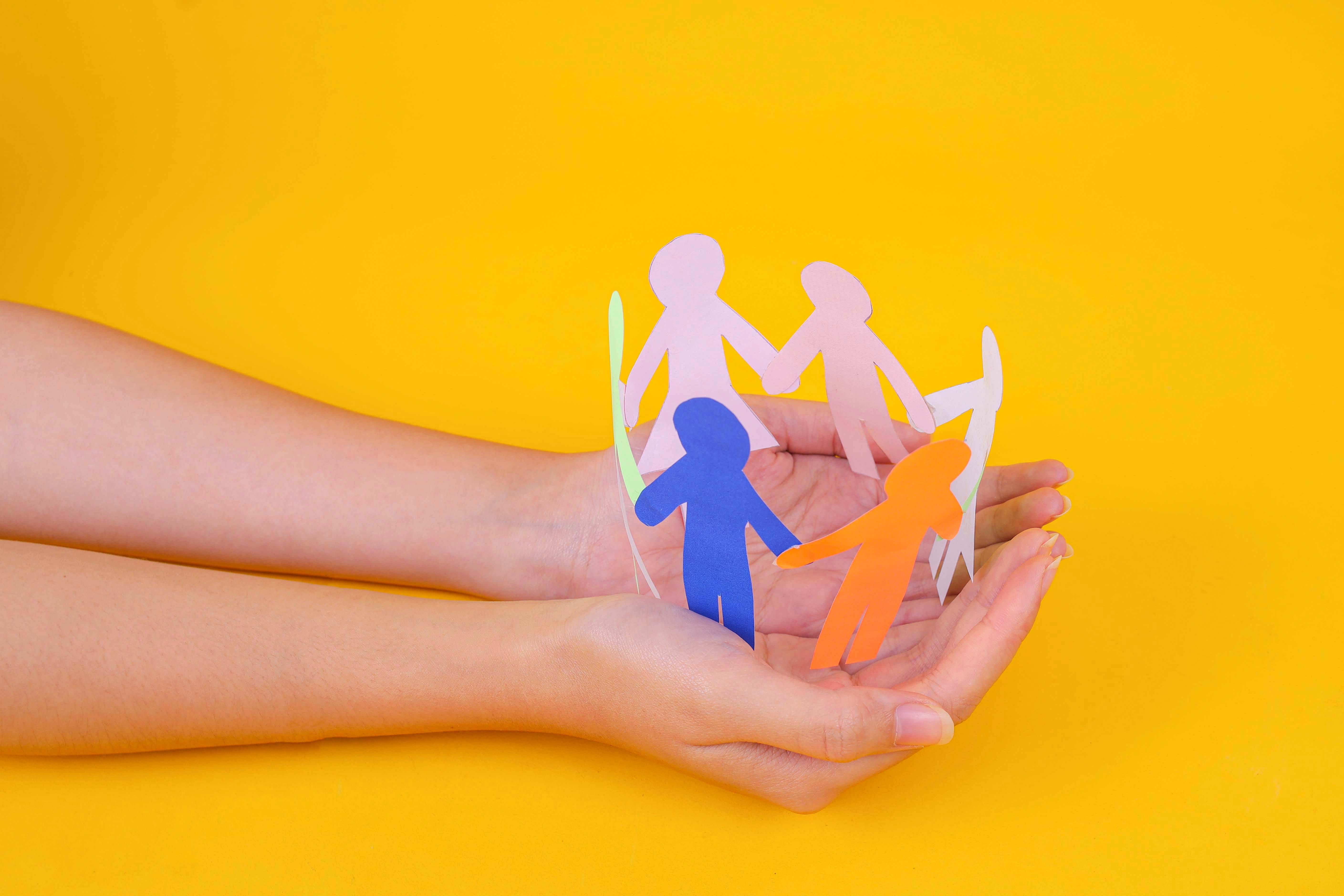 cupped hands holding paper figurines of people